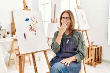 Middle age artist woman at art studio bored yawning tired covering mouth with hand. restless and...