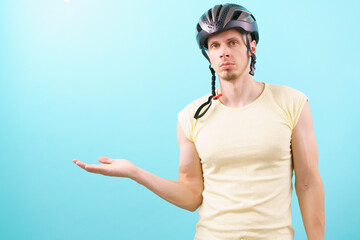 A caucasian man wearing a bicycle helmet points with his hands at an empty copy space on a blue background. Insurance. Injury. Protect. Secure. Protective. Perfect. Cycle. Accident. Guard. Hobbies