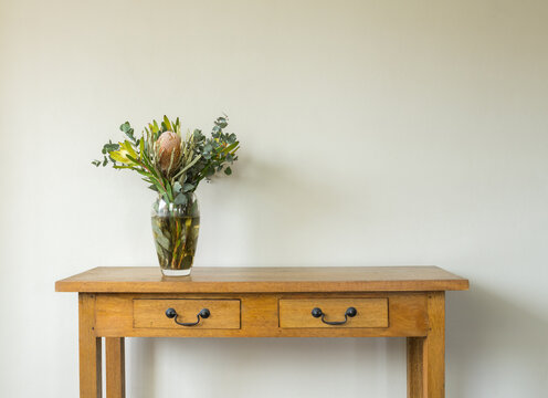 Australian native flowers in glass vase on oak side table against beige wall with copy space