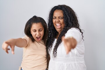 Mother and young daughter standing over white background pointing displeased and frustrated to the camera, angry and furious with you