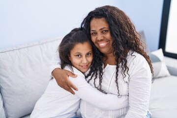Mother and daughter hugging each other sitting on sofa at home