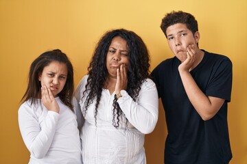 Family of mother, daughter and son standing over yellow background touching mouth with hand with...