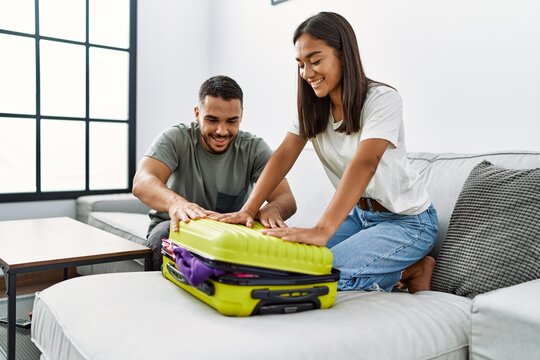 Latin man and woman couple smiling confident close travel suitcase at home