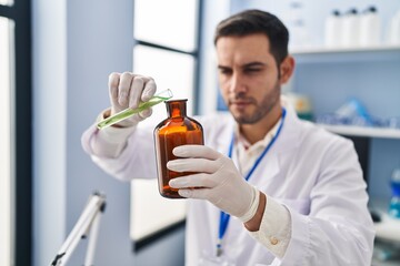 Young hispanic man scientist pouring liquid on bottle at laboratory