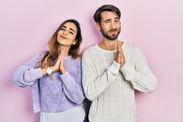 Young hispanic couple wearing casual clothes praying with hands together asking for forgiveness...