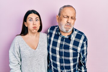 Hispanic father and daughter wearing casual clothes puffing cheeks with funny face. mouth inflated...