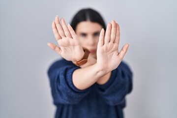 Young brunette woman standing over isolated background rejection expression crossing arms and palms...