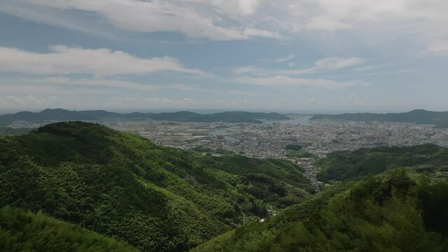 Rise up over green hills to reveal sprawling Kochi City in Shikoku, Japan