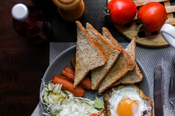 Breakfast, fried eggs, fried sausage, vegetable salad and toast on a brown wooden table with coffee.