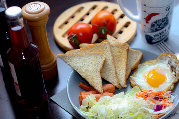 Breakfast, fried eggs, fried sausage, vegetable salad and toast on a brown wooden table with coffee.