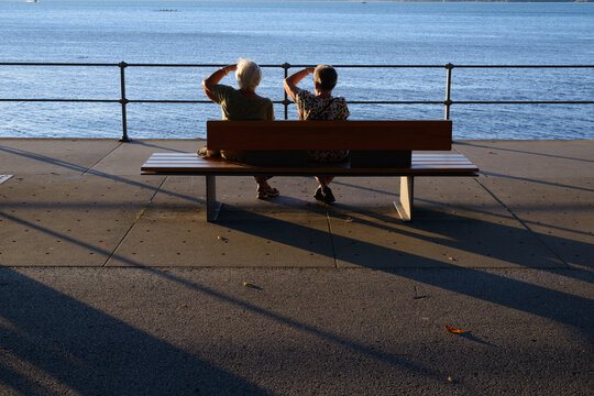 Two elderly friends siting on a bench, watching the lake against the low sun, copyspace