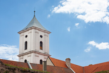 This shows The Church of the Raising of the Holy Cross in Osijek, Croatia. Looking up to the towers and roofline with blue sky and clouds above. - Powered by Adobe