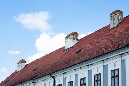 Look up at the cheerful red wood tile roof on the blue Baroque building in Osijek, Croatia. See three old chimneys.