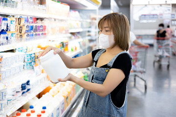 Beautiful woman wear a mask to prevent covid 19 making choice of products at supermarket. Focused female consumer shopping for groceries, selecting food, reading labels at modern mall