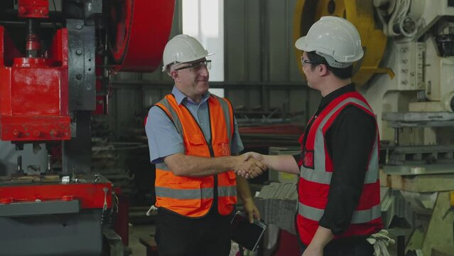 Two engineers, workers wearing safety uniforms and hard hats handshake in a factory. Caucasian men are 32, 48-year-old. Slow Motion