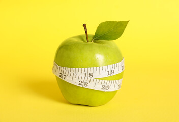 Fresh green apple with measuring tape on yellow background