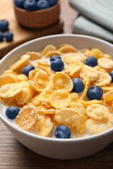 Bowl of tasty crispy corn flakes with milk and blueberries on wooden table, closeup
