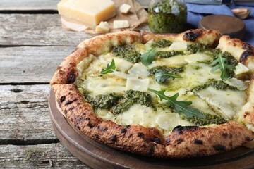 Delicious pizza with pesto, cheese and arugula on wooden table, closeup