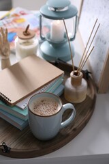Wooden tray with books, air reed freshener and cup of coffee on white table indoors