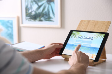 Man booking tickets online on tablet at white table, closeup. Travel agency concept