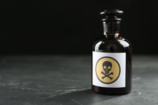 Glass bottle of poison with warning sign on black table. Space for text
