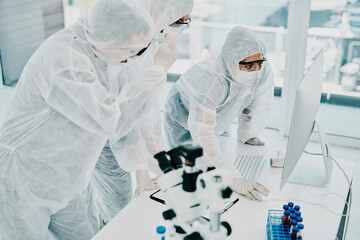 Group of doctors and scientists using computer for medical research on viruses dressed in hazmat...