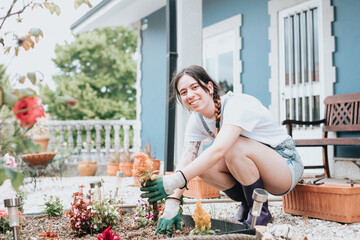 Cheerful young woman in gloves using gardening tools for planting flowers on back yard.casual clothes enjoying work at summer garden.Home garden new skills learning.Concept of gardening and floristics - Powered by Adobe