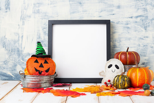 Halloween holiday concept with empty black frame and pumpkins on light table against a light wall. copy space,