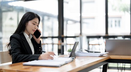 Concentrate businesswoman talking on mobile phone while analyzing weekly schedule in her notebook.