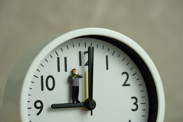 Miniature people toy figure photography. Reading routine concept. A men student standing read a book above clock