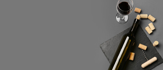 Bottle and glass of red wine with corks and opener on grey background with space for text