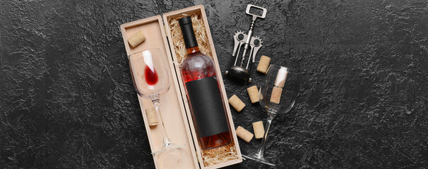 Box with bottle of red wine, glasses, corks and opener on dark background
