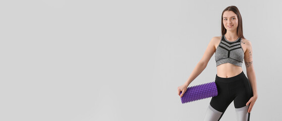 Sporty woman holding foam roller on grey background with space for text