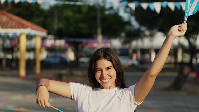  video of a girl with guayaquil city pennants in her hands in a park decorated for the independence and foundation celebrations, she waves the pennants while smiling on a sunny afternoon.
