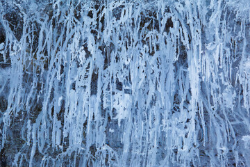Texture of winter ice on a stone cliff. Blue natural ice background