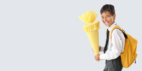 Happy little boy with school cone and backpack on light background with space for text