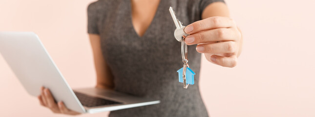 Female real estate agent with laptop and key on pink background, closeup