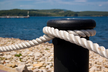 Fencing in the form of a black bollard with a rope on the background of the bay