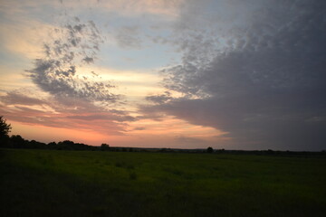 Naklejka na ściany i meble Clouds in a Sunset Over a Farm Field