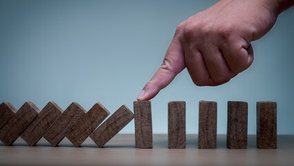 Hand stops the wooden cube block that is tilting down. Hedging concept or domino business crisis....