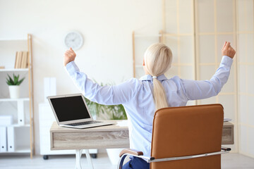 Mature businesswoman with back pain doing exercise in office