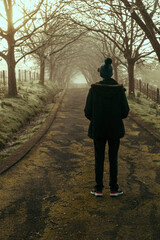 Back view of a young person standing alone on a road in winter with tree branches forming a tunnel in the distance