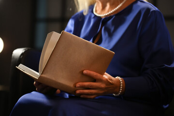 Mature woman reading old book at home late in evening, closeup