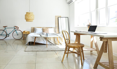 Interior of light bedroom with bicycle and workplace