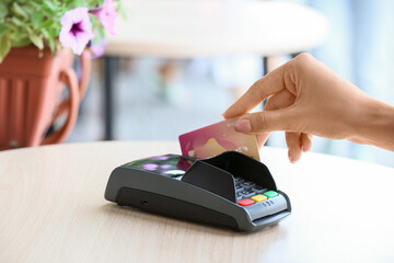 Woman paying with credit card via payment terminal at table in outdoor cafe, closeup