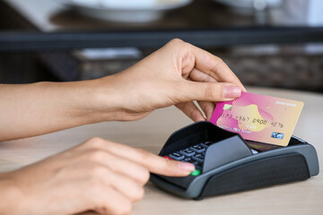 Woman paying with credit card via payment terminal at table in outdoor cafe, closeup