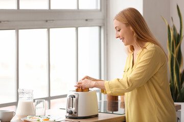 Mature woman making tasty toasts in kitchen