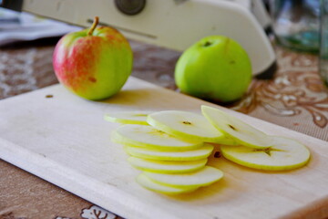 cut off by thin layer slices of apple for cooking and preparing close up wooden board on blurred background of kitchen table with tools. Selective focus
