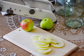 cut off by thin layer slices of apple for cooking and preparing wooden board on blurred background of kitchen table with tools. Selective focus
