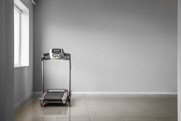 Modern treadmill near light wall in room